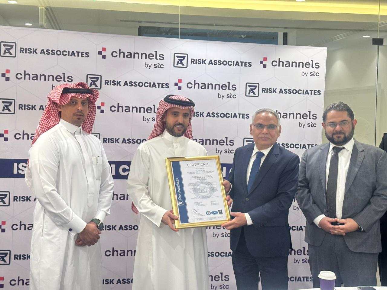 Group of professionals holding a framed certificate in front of a backdrop with "Risk Associates" and "Channels by stc" logos, representing recognition of excellence, certification achievement, and commitment to high standards in risk management services